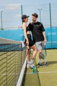 happy couple in active wear hugging while standing with rackets on tennis court, romance and sport t-shirt #665315756