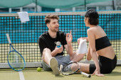 happy man chatting with woman and sitting near tennis net on court, sport, healthy lifestyle puzzle #665315838