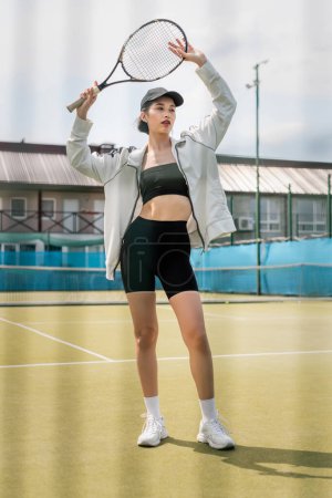 schöne Tennisspielerin in aktiver Kleidung und Mütze posiert mit Tennisschläger auf dem Platz, Sport und Mode