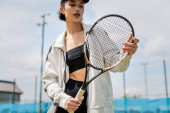 pretty woman in active wear and cap holding tennis racket on court, female tennis player, motivation Poster #665316116