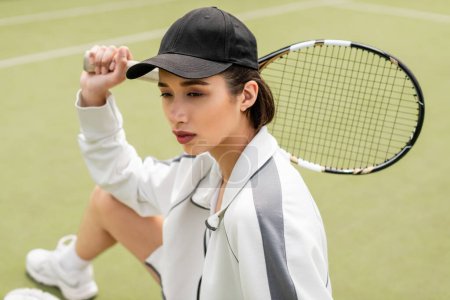 Photo for Portrait, woman in sportswear and cap sitting on tennis court, holding racket, female tennis player - Royalty Free Image