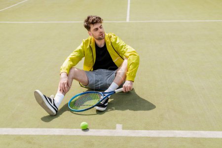 przystojny mężczyzna w aktywnym ubraniu spoczywa na korcie tenisowym, męski tenisista z rakietą, sport