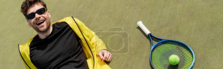 Téléchargez les photos : Bannière, homme heureux dans des lunettes de soleil reposant près de balle de tennis et raquette, joueur de tennis, sport et style - en image libre de droit