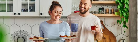 Mujer positiva sosteniendo platos con desayuno cerca de novio con té en la cocina en casa, pancarta