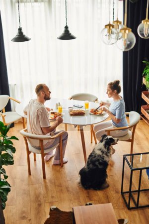 Side view of cheerful couple having homemade breakfast near border collie dog at home in morning mug #665725916