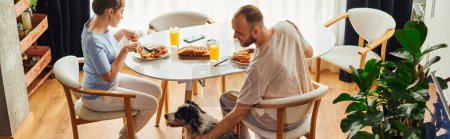 Smiling man in homewear petting border collie while having breakfast with girlfriend at home,banner