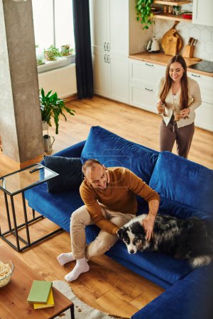 High angle view of smiling woman holding coffee while boyfriend petting border collie at home