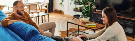Lächelnde Frau streichelt Border Collie Hund auf Couch neben Freund im Wohnzimmer, Banner