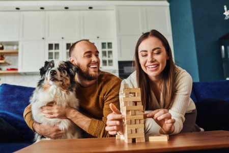 Mujer sonriente jugando bloques de madera juego cerca de novio y frontera collie en sala de estar en casa