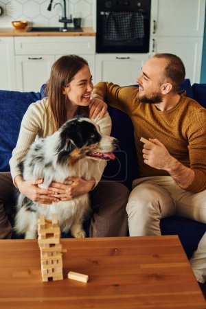 Joyful couple talking while spending time with wood blocks game and border collie at home