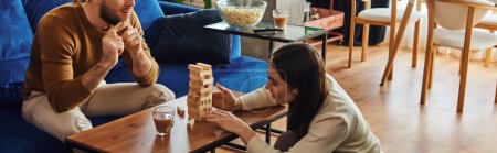 Woman playing wood blocks game with boyfriend near popcorn and coffee at home,banner