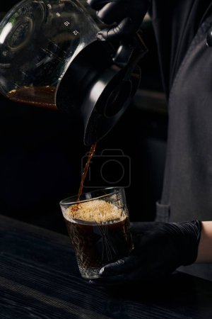 barista pouring aromatic espresso from coffee pot into crystal glass, alternative brewing method
