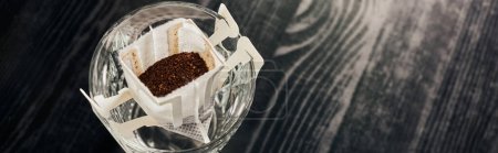 Foto de Vidrio con café molido aromático en bolsa de filtro sobre mesa negra, método de elaboración de cerveza vertido, pancarta - Imagen libre de derechos