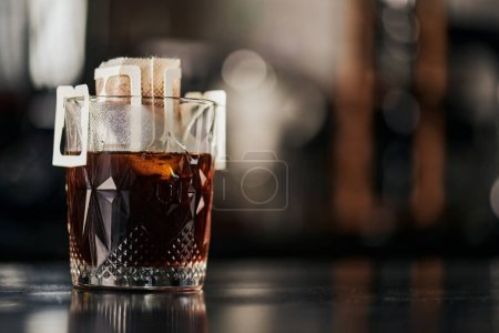 szkło kryształowe, kawa mielona w papierowym worku filtracyjnym na czarnym drewnianym stole w kawiarni, metoda kroplówki espresso
