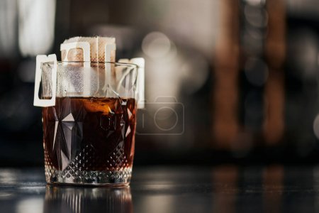 Kristallglas, gemahlener Kaffee in Papierfiltertüte auf schwarzem Holztisch im Café, Espresso-Tropfmethode