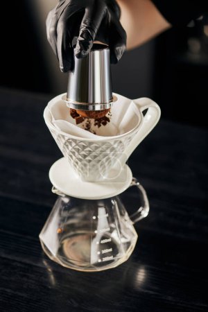 Barista gießt feinmahlenen Kaffee aus Rührwerk in Keramiktropfer auf Glaskanne, Espresso im Stil V-60