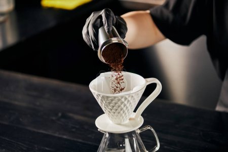 Barista gießt feinen gemahlenen Kaffee von einer Rührvorrichtung in einen Keramiktropfer und bereitet Espresso im Stil von V-60 zu