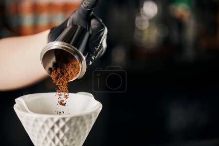 Photo for Barista preparing V-60 style espresso, pouring fine grind coffee from jigger into ceramic dripper - Royalty Free Image