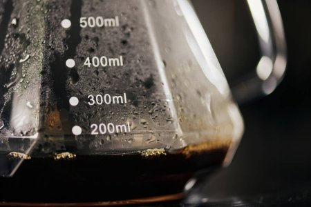 vista de cerca del espresso negro recién hecho en una cafetera de vidrio con escala de medición, método de goteo