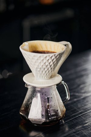 ceramic dripper with pour-over coffee on glass pot in cafe on black table, alternative V-60 style 