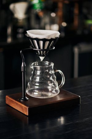 drip holder with filter bag, glass coffee pot on black wooden counter, alternative V-60 style method