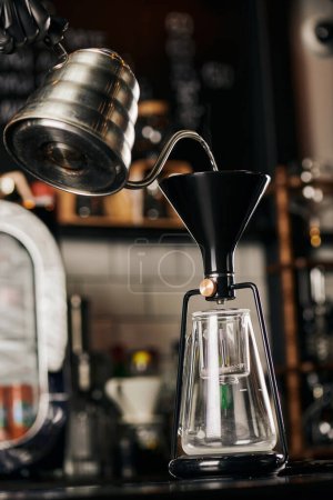 Teilansicht eines Barista, der kochendes Wasser in eine Kaffeemaschine im Café gießt