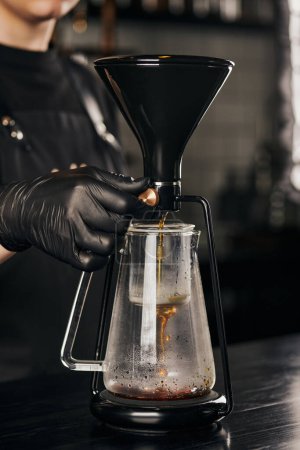 Photo for Barista in black latex glove regulating siphon coffee maker while brewing natural pour-over espresso - Royalty Free Image