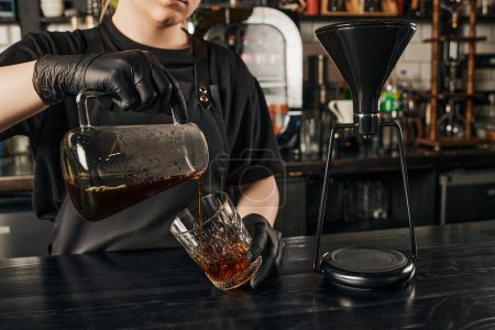 Teilansicht des Barista, der frischen Espresso in Kristallglas in der Nähe der Siphon-Kaffeemaschine im Café gießt