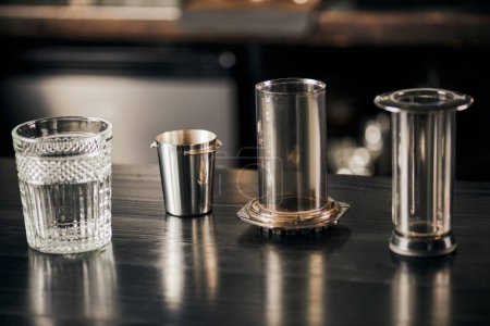 crystal glass and parts of aero press coffee maker on black wooden table in modern cafe