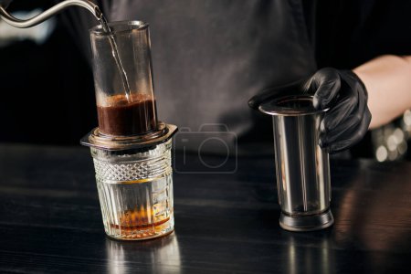 partial view of barista pouring boiling water in aero press coffee maker, alternative espresso method