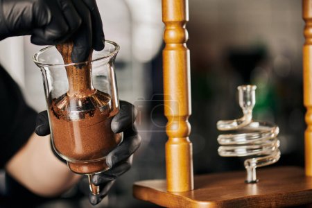 partial view of barista pressing ground coffee with tamper in cold brew coffee maker, alternative method