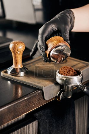 Ausgeschnittene Ansicht des Barista mit Stampfer und Portafilter mit aromatischem Kaffee im Café