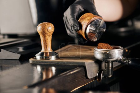 cropped view of barista holding tamper near portafilter with ground coffee, espresso preparation