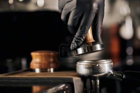 coffee shop, cropped view of barista in black latex glove holding tamper near portafilter