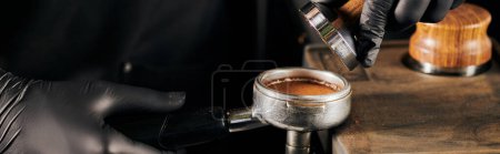 Foto de Vista parcial de barista en guantes negros presionando café molido en portafilter, cafetería, pancarta - Imagen libre de derechos