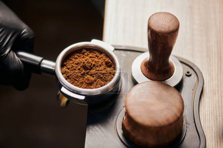 barista holding portafilter with grinded coffee, tamper, cafe, alternative brew, top view 