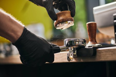 abgeschnittene Ansicht des männlichen Barista mit Stampfer und Portafilter mit gemahlenem Kaffee, Espresso zubereiten 