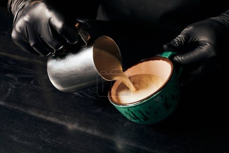Foto de Parcial, barista en guantes de látex preparando capuchino, espresso, latte art, jarra con leche - Imagen libre de derechos