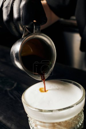barista en guantes de látex preparando latte macchiato, vertiendo espresso, jarra con café, macro