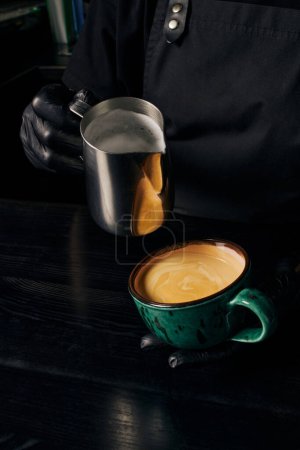 Barista bereitet Cappuccino zu, hält Kanne mit Milch, Tasse mit Espresso, Arabica, Energie 