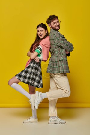 glückliches stilvolles Paar, Rücken an Rücken stehend, posierend auf gelbem Hintergrund, Studentenoutfit, Jugend