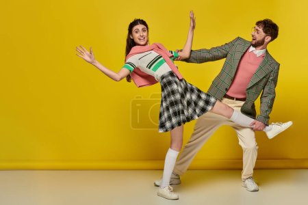 cheerful man in glasses catching falling woman, young couple, funny, yellow backdrop, emotional