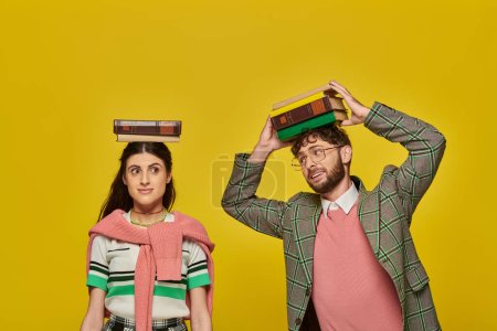 couple of students, happy young man and woman standing with books on heads on yellow backdrop, youth