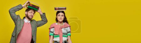 Photo for Couple of students, happy young man and woman standing with books on heads, yellow backdrop, banner - Royalty Free Image