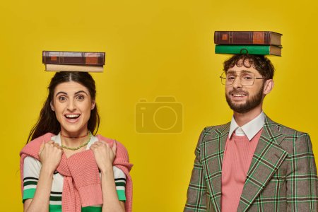 couple of students, happy man and excited woman standing with books on heads, yellow backdrop, young