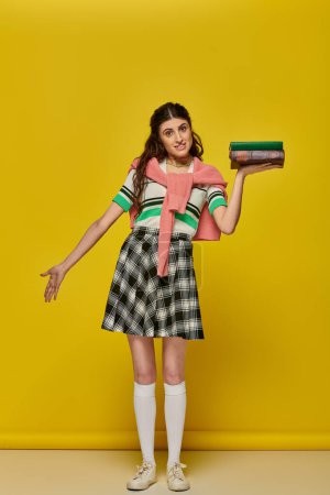 Photo for Young student with books, brunette woman in checkered skirt posing on yellow backdrop, brunette - Royalty Free Image
