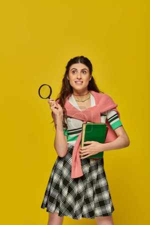 Photo for Curious young woman holding books and magnifier, zoom, discovery, student in college outfit, smile - Royalty Free Image