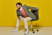 emotional and bearded man screaming and sitting on office chair, yellow backdrop, angry student Stickers #667826710