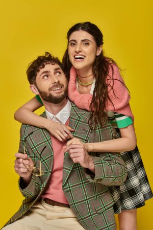 excited woman hugging bearded man, holding glasses, yellow backdrop, college outfits, students