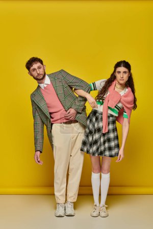 Foto de Estudiantes divertidos, pareja de pie sobre fondo amarillo, hombre y mujer en trajes universitarios, ropa académica - Imagen libre de derechos